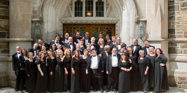 The group in black suits and gowns smiling in front of an old building