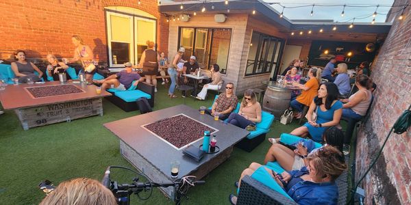 People socializing in a cozy outdoor patio with fire pits and string lights.