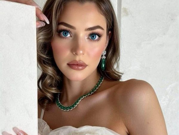 Elegant woman with striking blue eyes wearing emerald jewelry and a white dress.