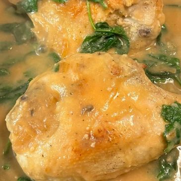 Close-up of cooked chicken thighs in creamy sauce with spinach.