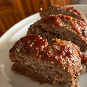 Close-up of sliced meatloaf with ketchup on a white plate.
