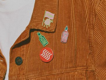 Corduroy jacket with colorful enamel pins attached.