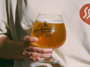 Person holding a glass of beer with a logo on it.