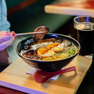 A bowl of ramen with boiled eggs and pork held by chopsticks.