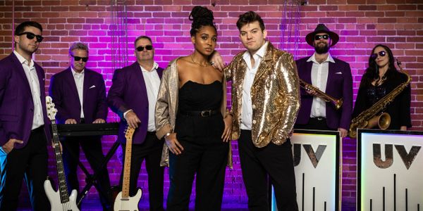 A band of musicians stands in front of a brick wall. 