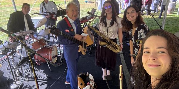 A woman takes a selfie that features a band of musicians on stage, getting ready to perform