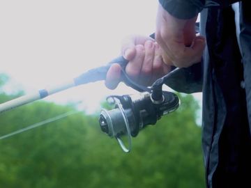 A close up view of a fishing reel in the hands of Bobby's guest with trees in the background.