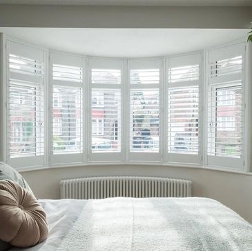 White plantation shutters in a bedroom bay window. Designed perfectly with midrails and 63mm louvres