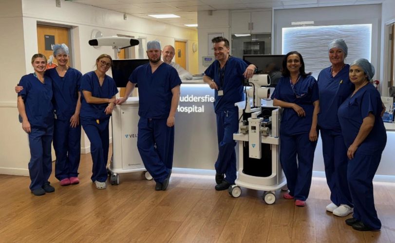 Medical team in blue scrubs posing with hospital equipment.