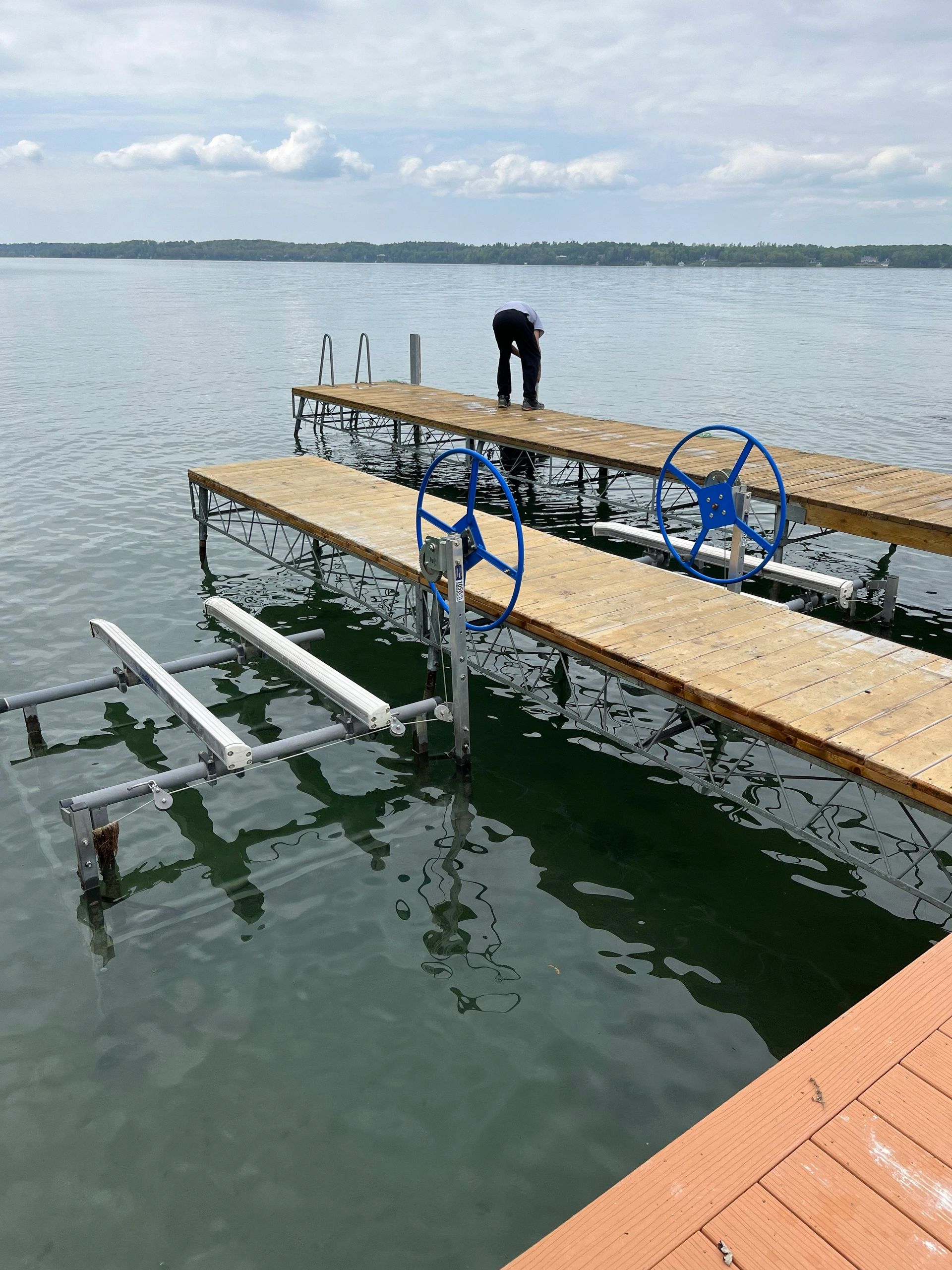A person bending over on a wooden dock by a calm lake.