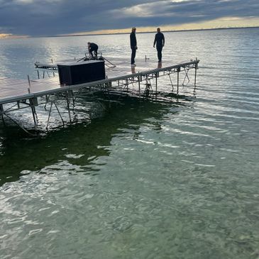 Three people on a dock over clear water at sunset with cloudy sky.