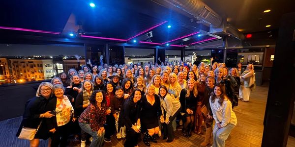 Large group of women gathered on a rooftop at night, smiling for a photo.