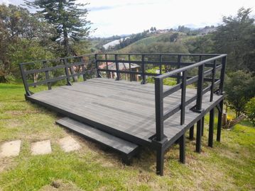 A wooden deck with black railings on a grassy hill overlooking a scenic landscape.