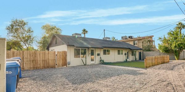 Single-story house with a gravel driveway and fenced yard under a clear sky.