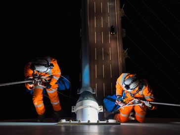 Two workers in orange safety gear rappelling down a tall structure at night.