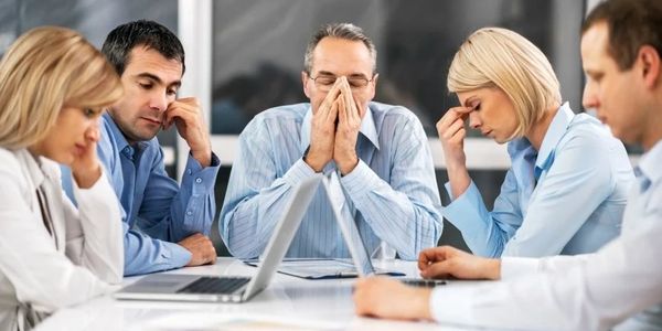 A group of stressed professionals in a meeting looking worried and overwhelmed.