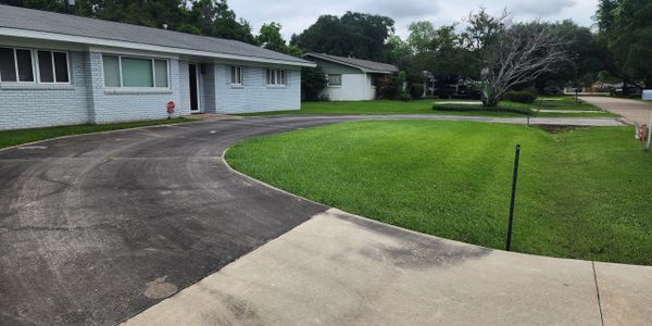 Curved asphalt driveway leading to a white brick house with a green lawn.