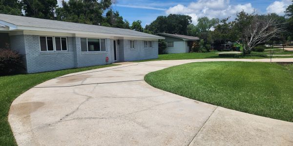 Curved driveway leading to a single-story brick house with a green lawn.