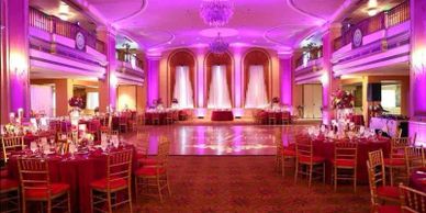 Elegant ballroom decorated with purple lighting and round tables.