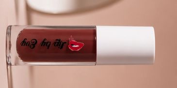 A brown liquid lipstick with a white cap and a lip print on the label.