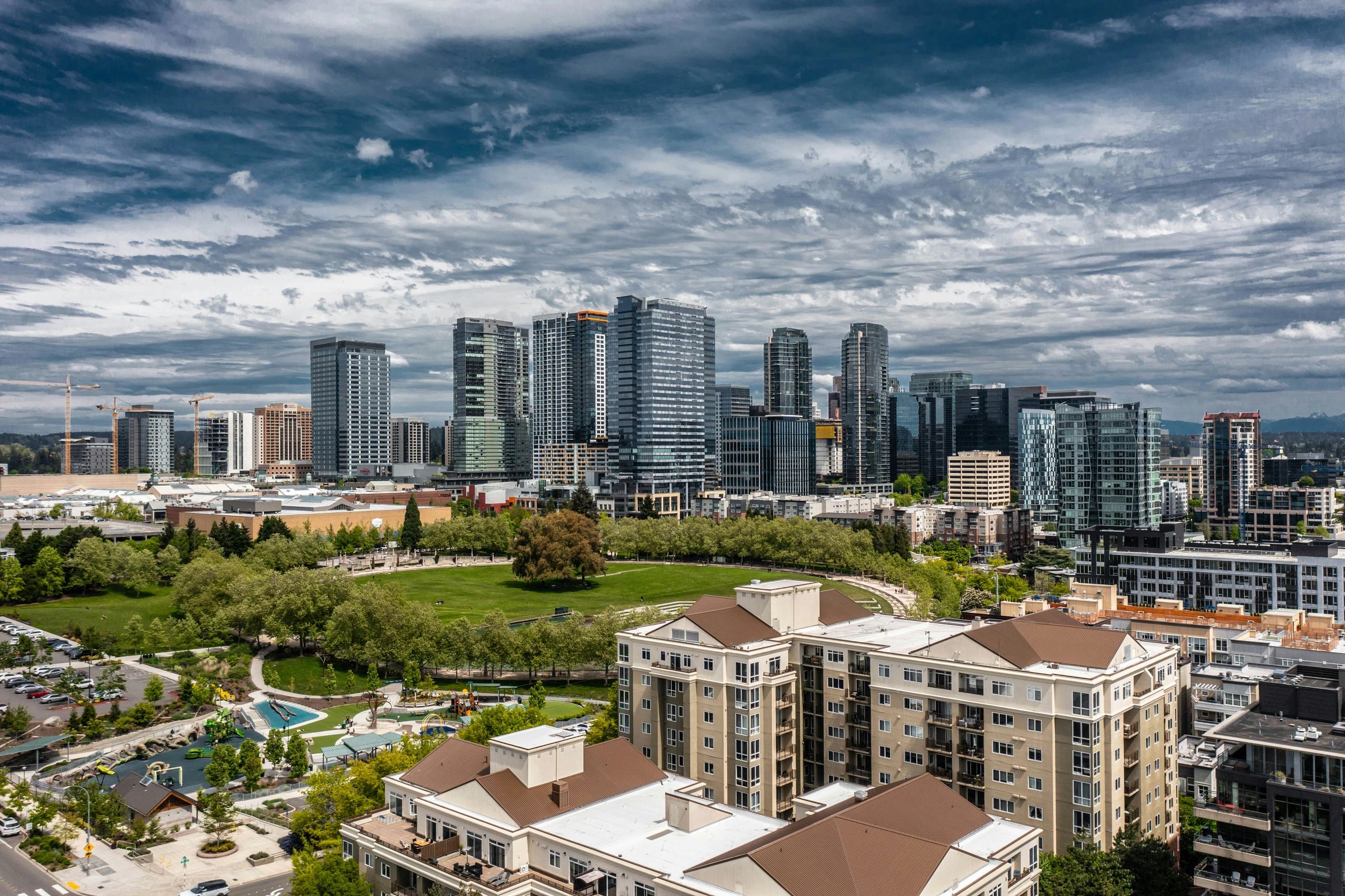 Modern city skyline with green park under a dramatic cloudy sky.