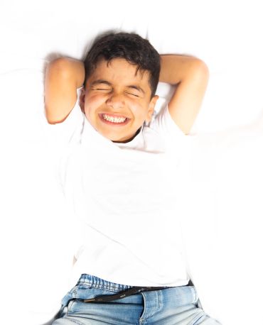 Smiling boy with eyes closed, lying back with hands behind head.