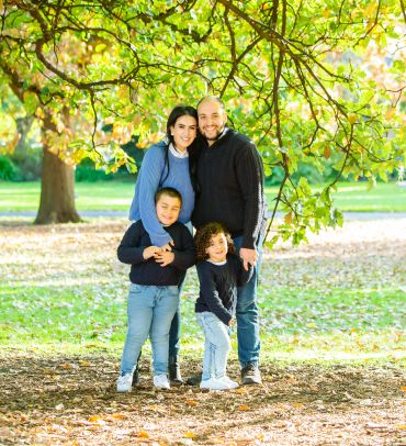 Happy family posing outdoors under tree branches.