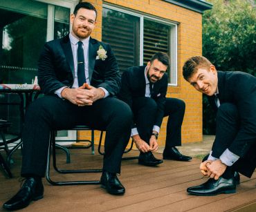 Three groomsmen fixing shoes and posing outdoors.