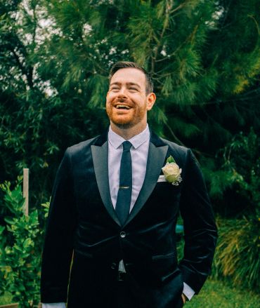 Man in tuxedo smiling outdoors.