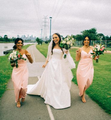 Bride and two bridesmaids joyfully walking outdoors.