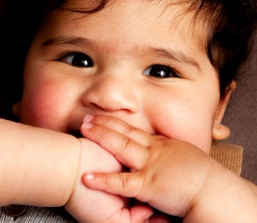 Close-up of a baby with hands near mouth.