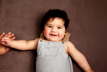 Smiling baby holding an adult's hand while lying down.