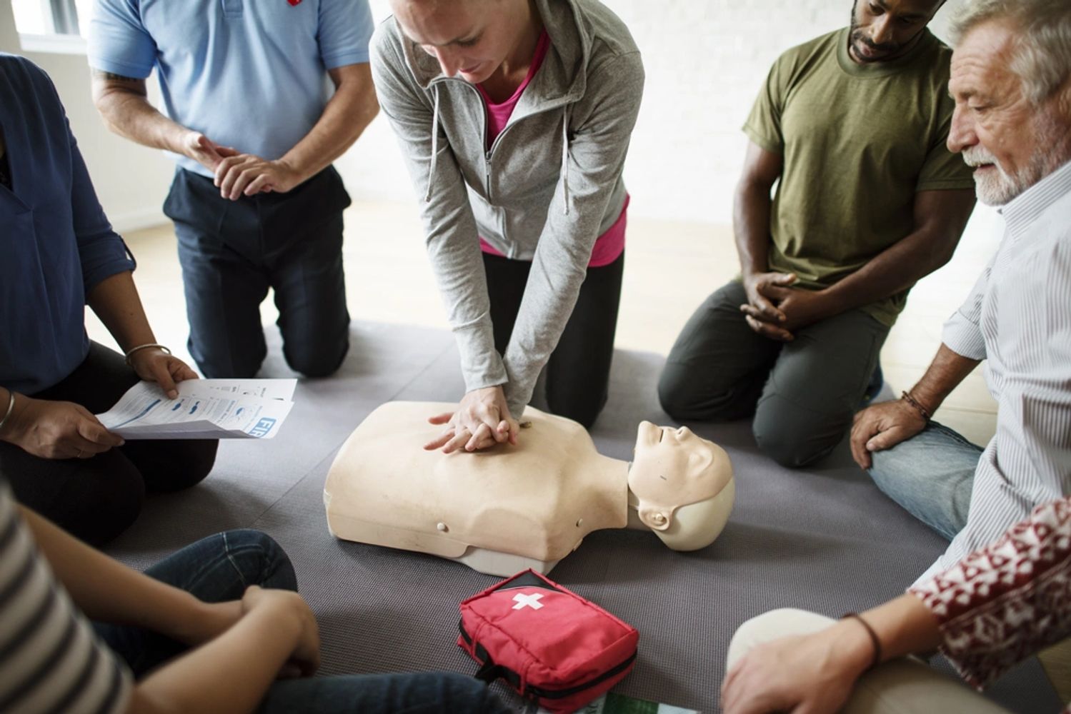 A CPR class with one person performing CPR on a manikin while others in the class watch.