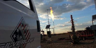 Gas flare burning at an industrial site near a Silverline vehicle.