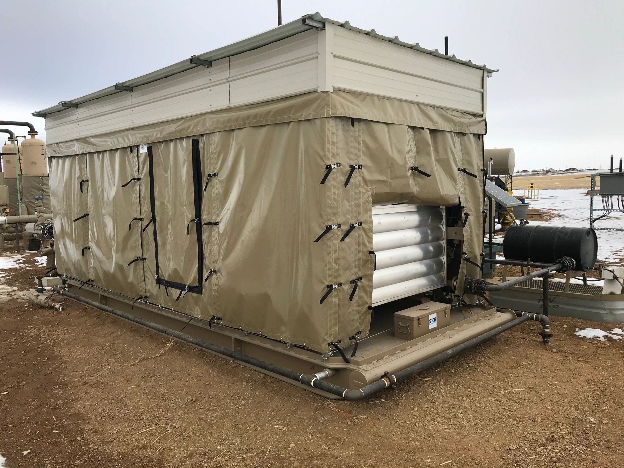 Industrial equipment covered with beige tarps on a snowy day.