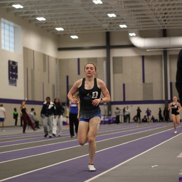 Female athlete sprinting indoors on a track.