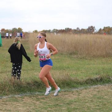 Female runner competing in a cross-country race on a grassy trail.