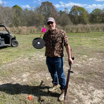 Man holding a sword and archery target in a field.