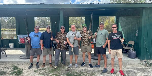 Group of men holding rifles outdoors under shelter.