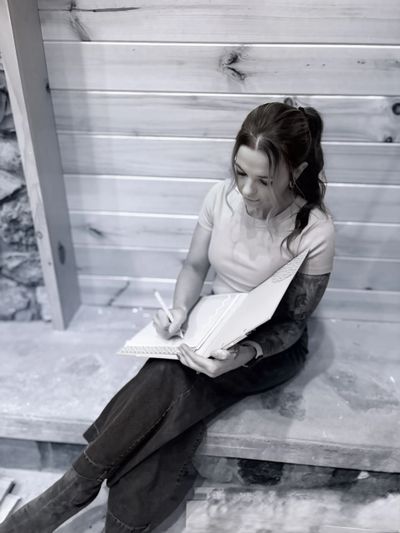 Woman sitting and writing in a notebook on a wooden bench.