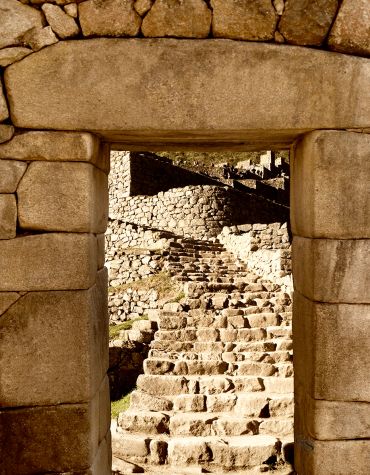 Ancient stone doorway framing a rugged staircase in a sunlit ruin.