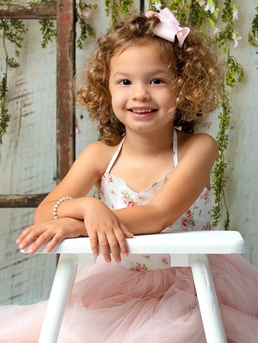Studio portrait of a toddler girl with curly hair wearing a pink dress and a pearl bracelet.