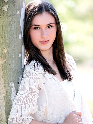 Outdoor Senior portraits pretty young girl wearing white blouse standing against tree