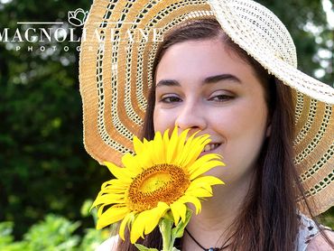 Senior pictures young woman wearing a hat holding a yellow sunflower.