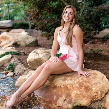 Outdoor senior pictures pretty girl with long brown hair in a pink dress with roses in her lap.