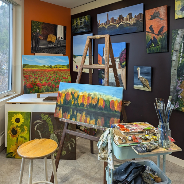 Photo of the artist's studio - a lively, colorful and light space; walls and easel full of paintings