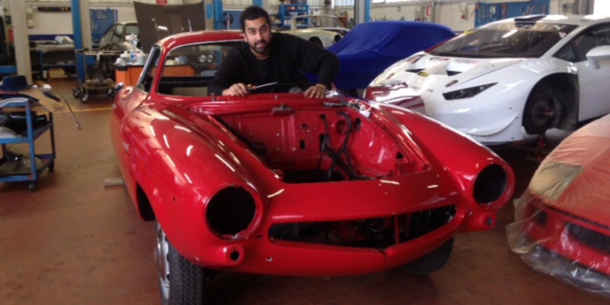 Man working on a red vintage car without headlights.