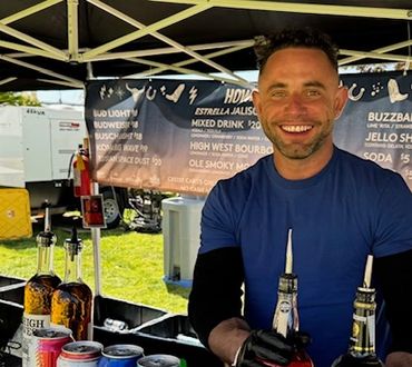 Smiling bartender serving drinks at an outdoor booth.
