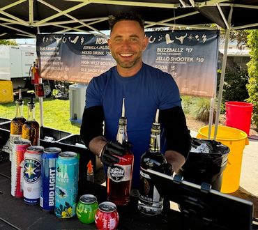 Smiling bartender serving drinks at an outdoor booth.