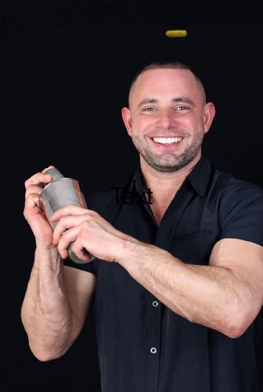 Smiling man shaking a cocktail shaker against a black background.